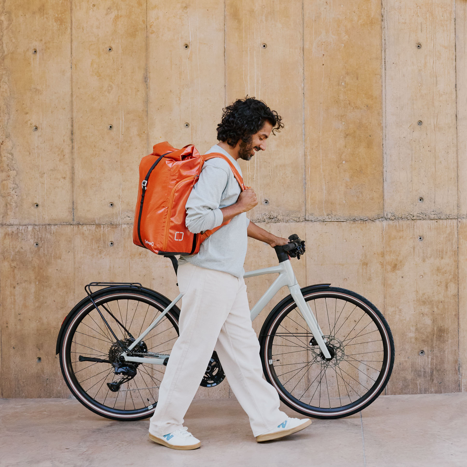 Einer Person mit einer Fahrradtasche von der Marke otinga auf dem Rücken, der ein Fahrad schiebt.